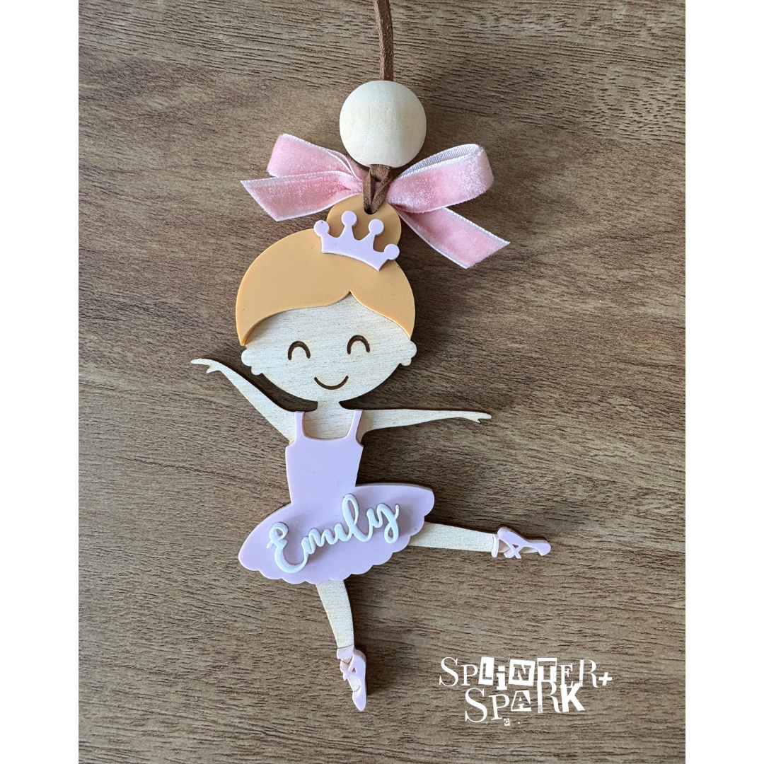 Decorative ballerina ornament with a pink bow on a wooden surface, branded 'Splinter Spark'.