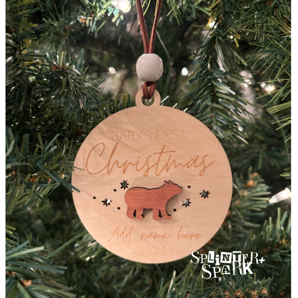 Wooden ornament with 'Baby's First Christmas' text and bear design, hanging on a tree.