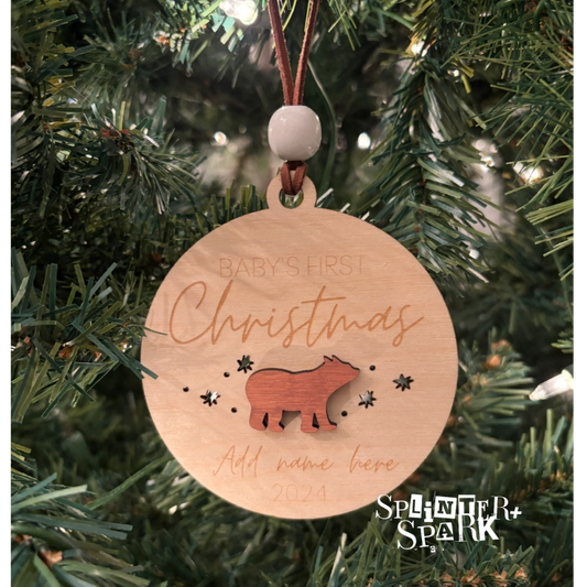 Wooden ornament with 'Baby's First Christmas' text and bear design, hanging on a tree.