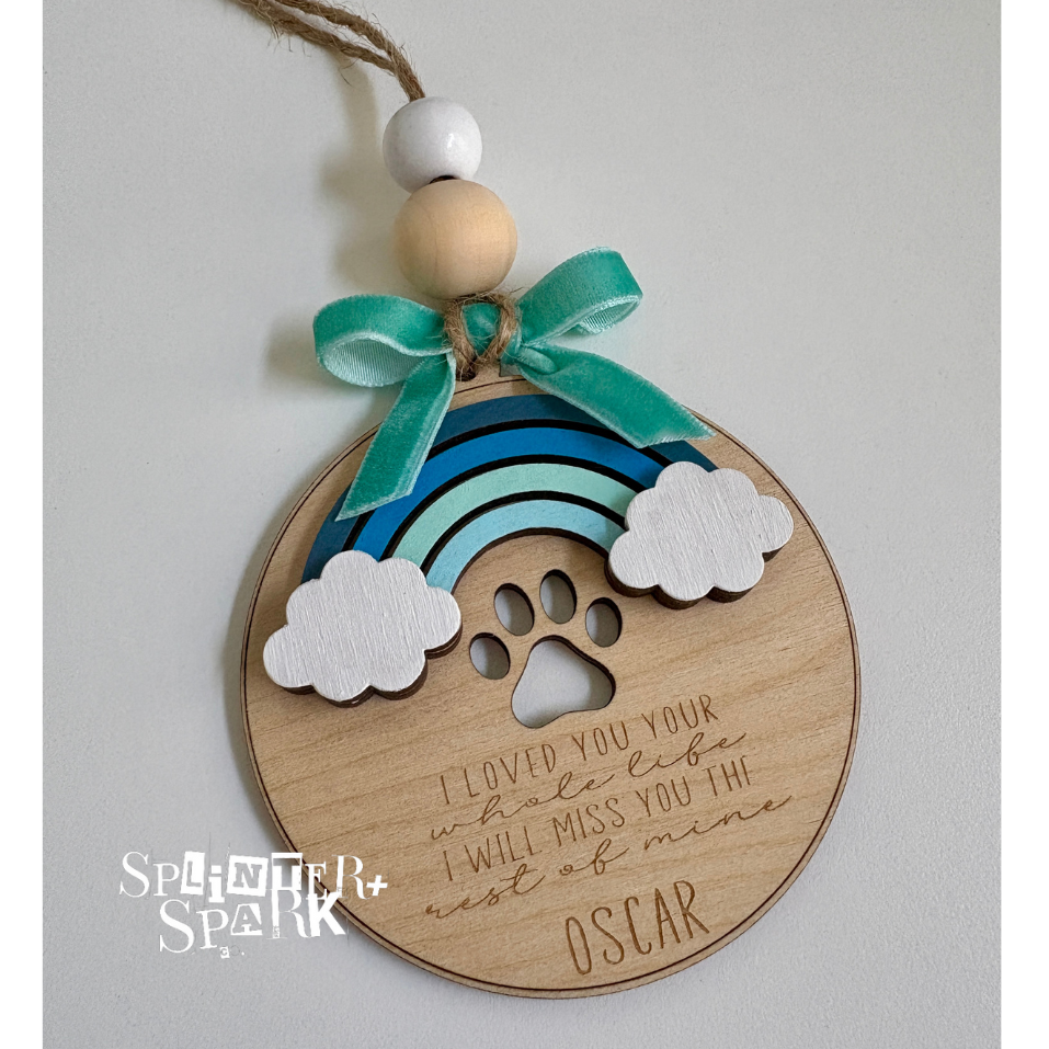 Wooden ornament with rainbow, paw print, and text on a gray background